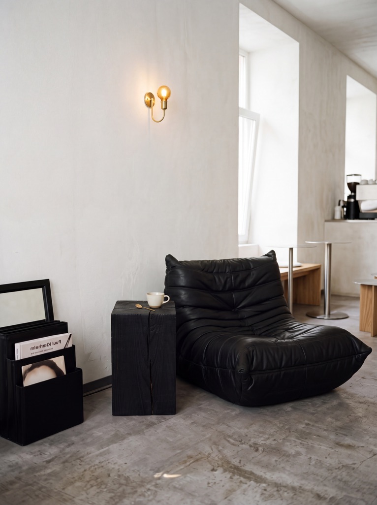 A timber block side table alongside a black lounge chair in a sunlit café